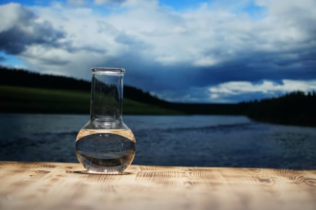 Clean water in lab flask against nature background