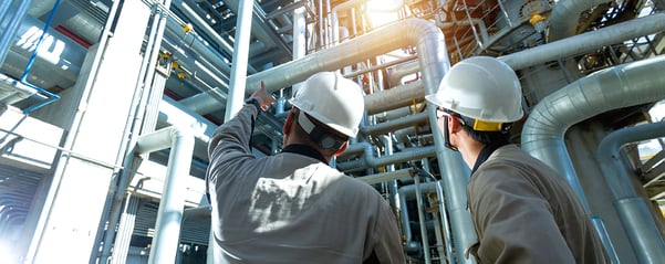 Two technicians in the fluid systems engineering and assembly service industry talk about a current project in front of fluid systems piping.
